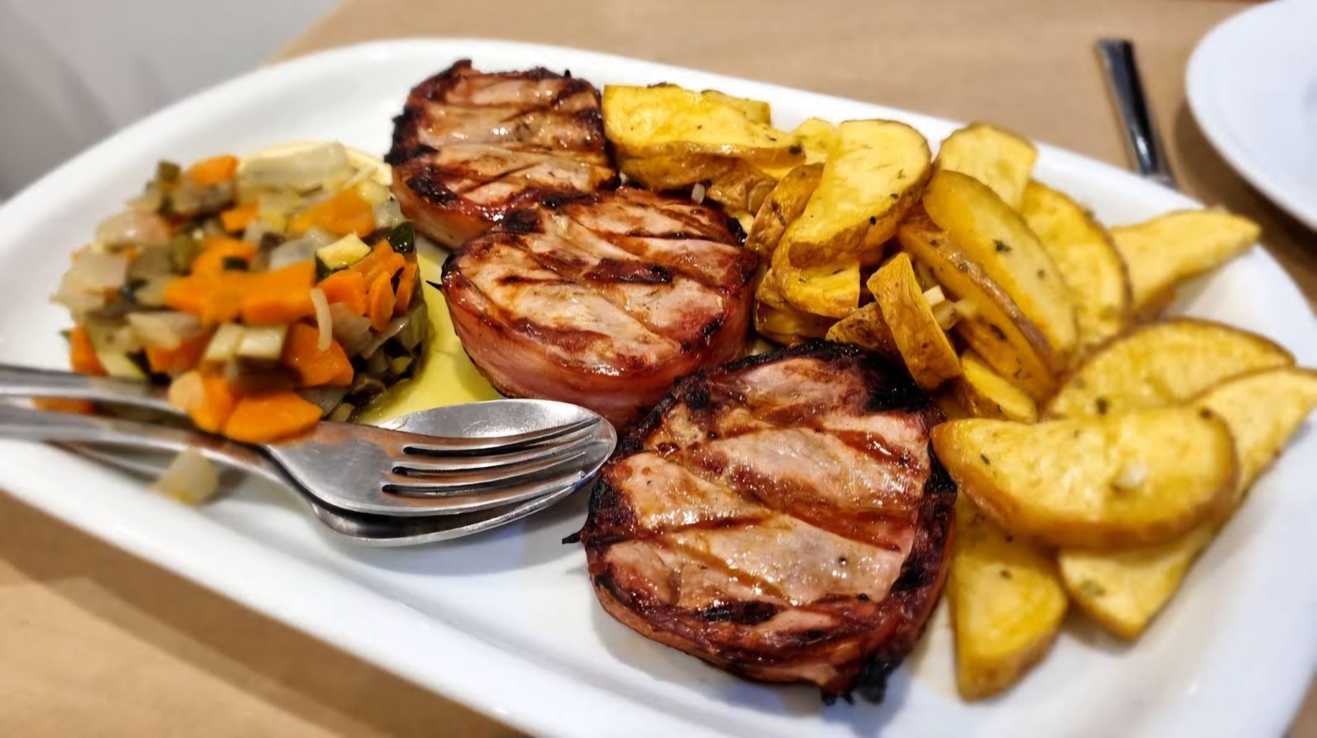 Um prato de comida com carne, batatas e vegetais sobre uma mesa.