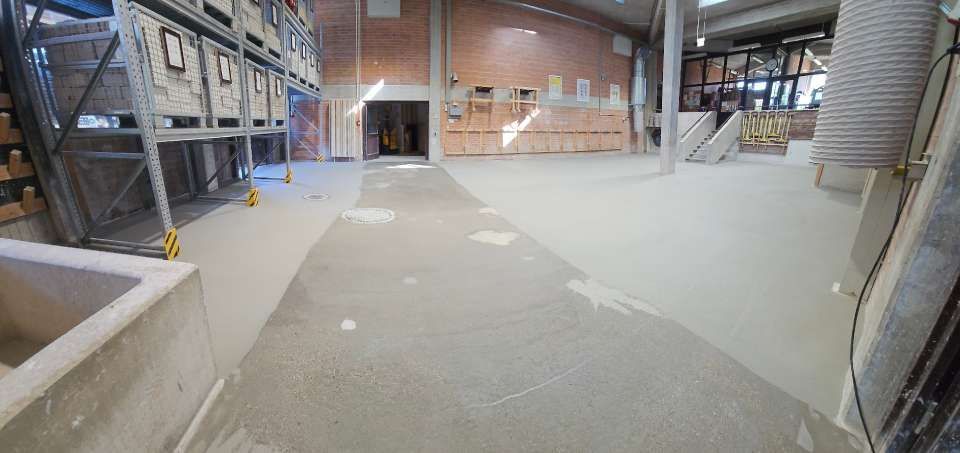 Innenansicht einer Lagerhalle mit Betonboden, Metallregalen und Ziegelwänden.