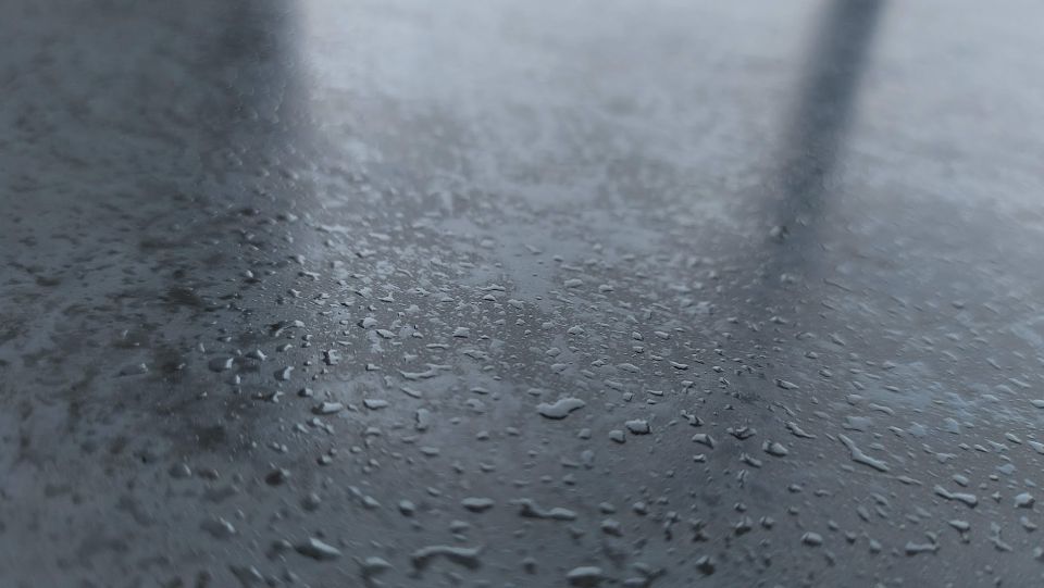 Wassertropfen auf einer dunklen, reflektierenden Oberfläche, möglicherweise einer Arbeitsplatte, mit Lichtreflexionen.