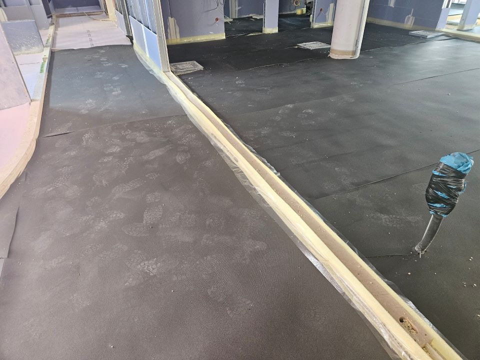 Eine Baustelle mit freiliegendem Boden. Ein langer, heller Trog verläuft durch die Mitte. Dunkler Bodenbelag erstreckt sich über den gesamten Bereich.