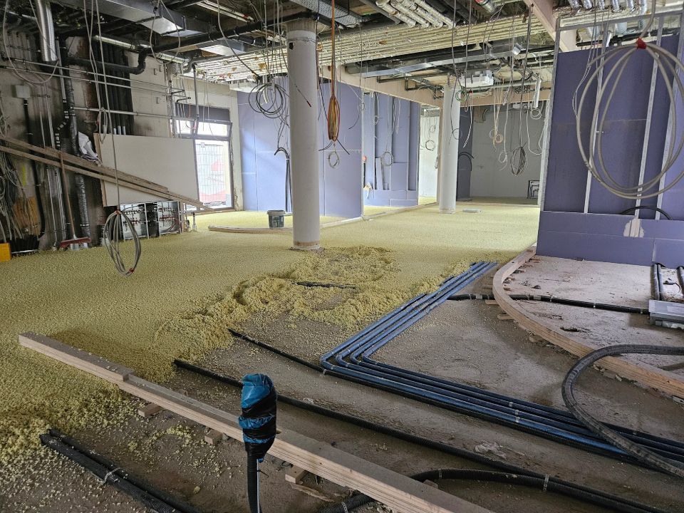 Innenansicht einer Baustelle mit gelber Dämmung auf dem Boden, Verkabelung und teilweise errichteten Wänden.