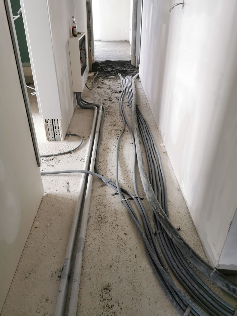 Flur im Bau, graue Elektrokabel und Leitungen auf dem Betonboden.