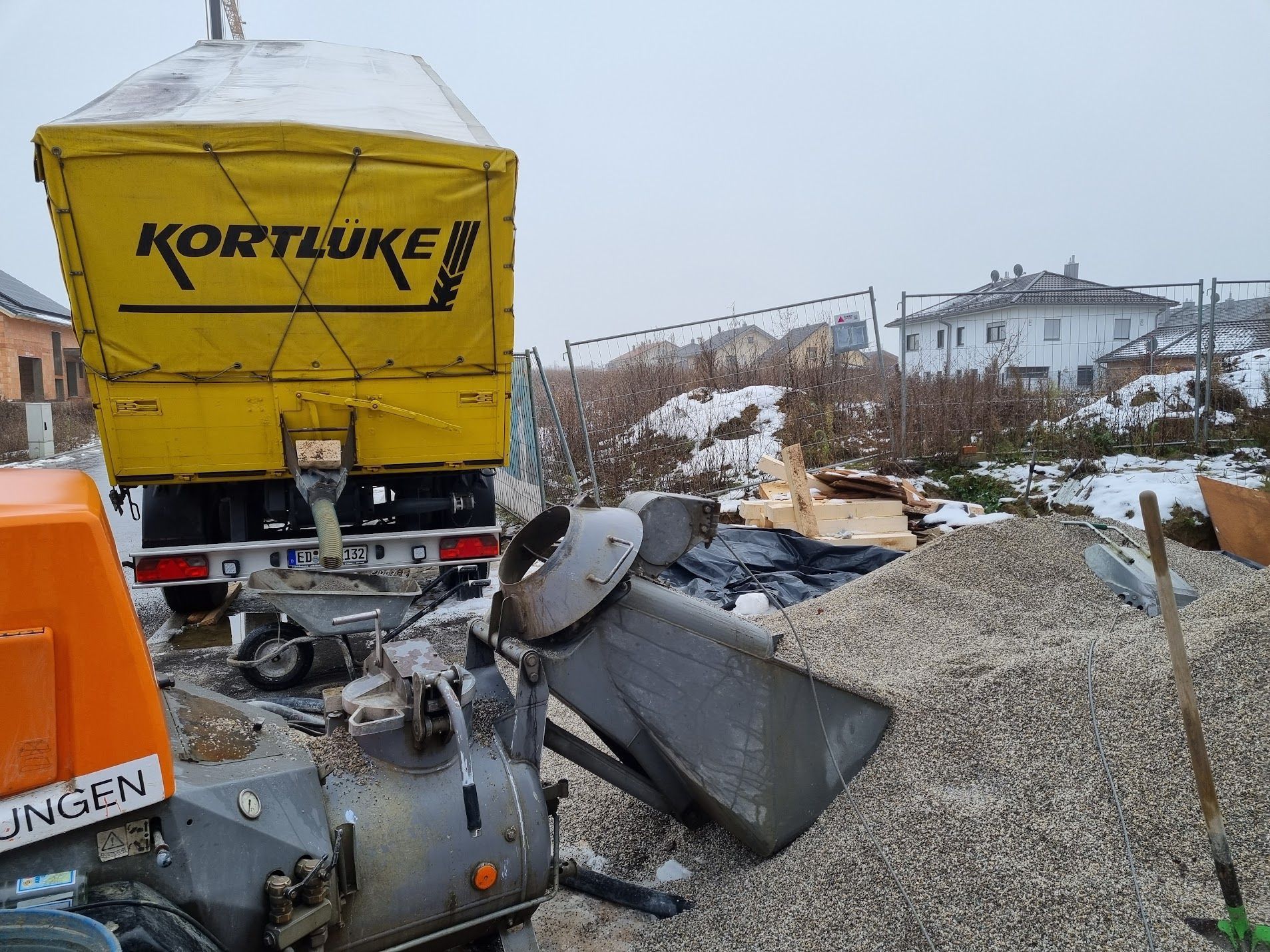 Ein gelber LKW mit dem Logo „KORTLUKE“ kippt in einer verschneiten Außenlandschaft Kies auf einen Haufen.
