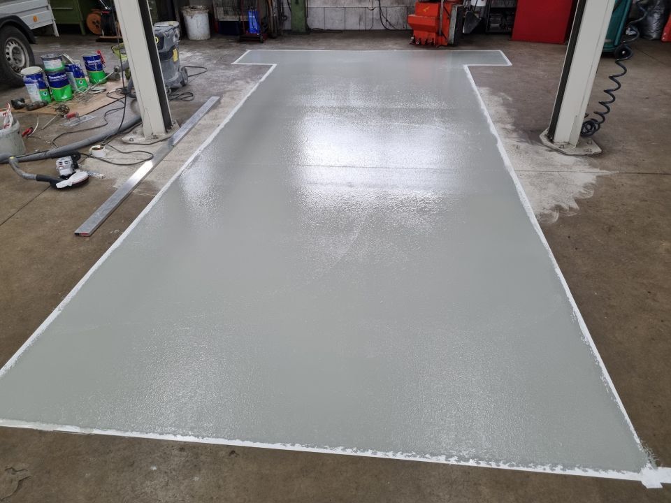 Frisch gestrichener, hellgrauer Betonboden in einer Werkstatt mit weißen Bordüren und Hebebühnenstützen.