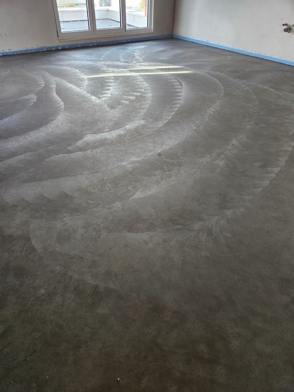 Betonboden mit kreisförmigen, helleren Markierungen in einem unfertigen Raum.