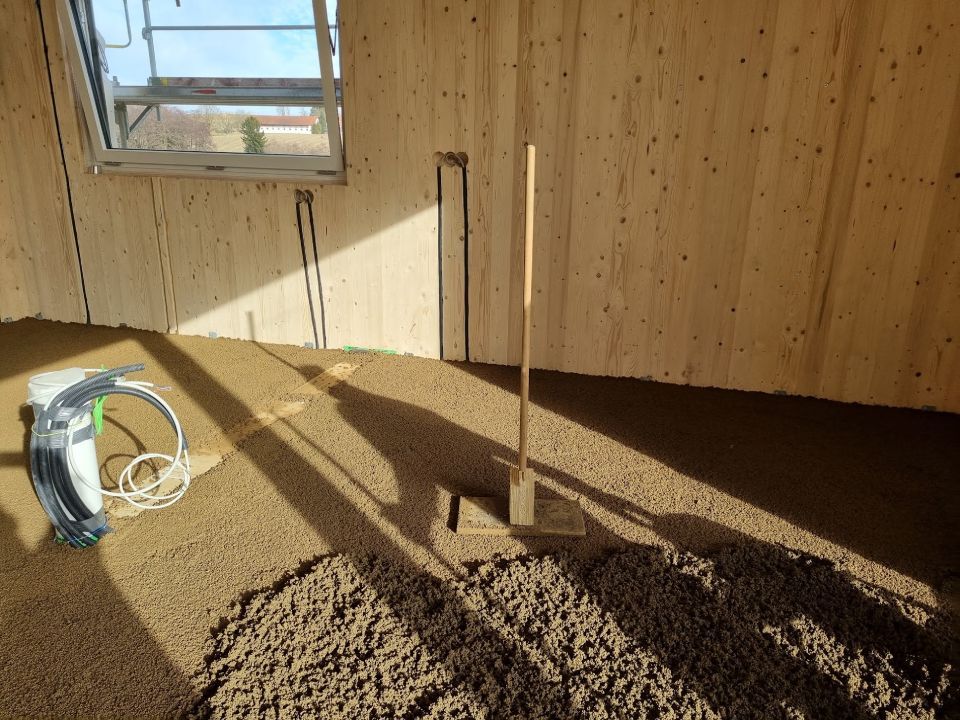 Innenausbau mit Holzwänden, Boden aus braunem Material und einer stehenden Kelle.