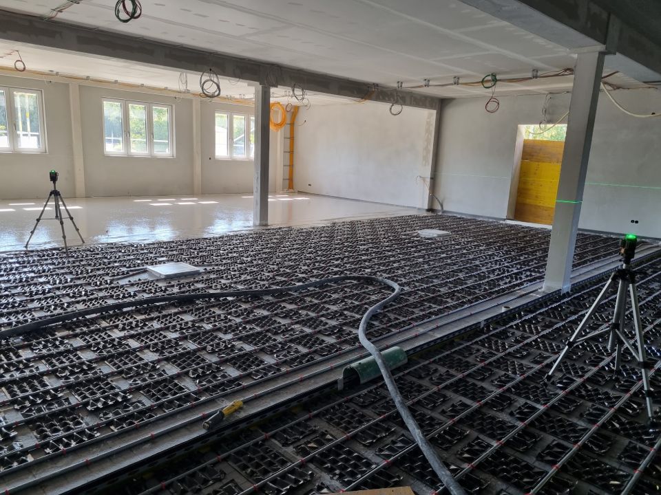 Innenansicht eines Dachbodens mit einem gitterartigen Bodensystem für die Fußbodenheizung. Holzbalken an der Decke.