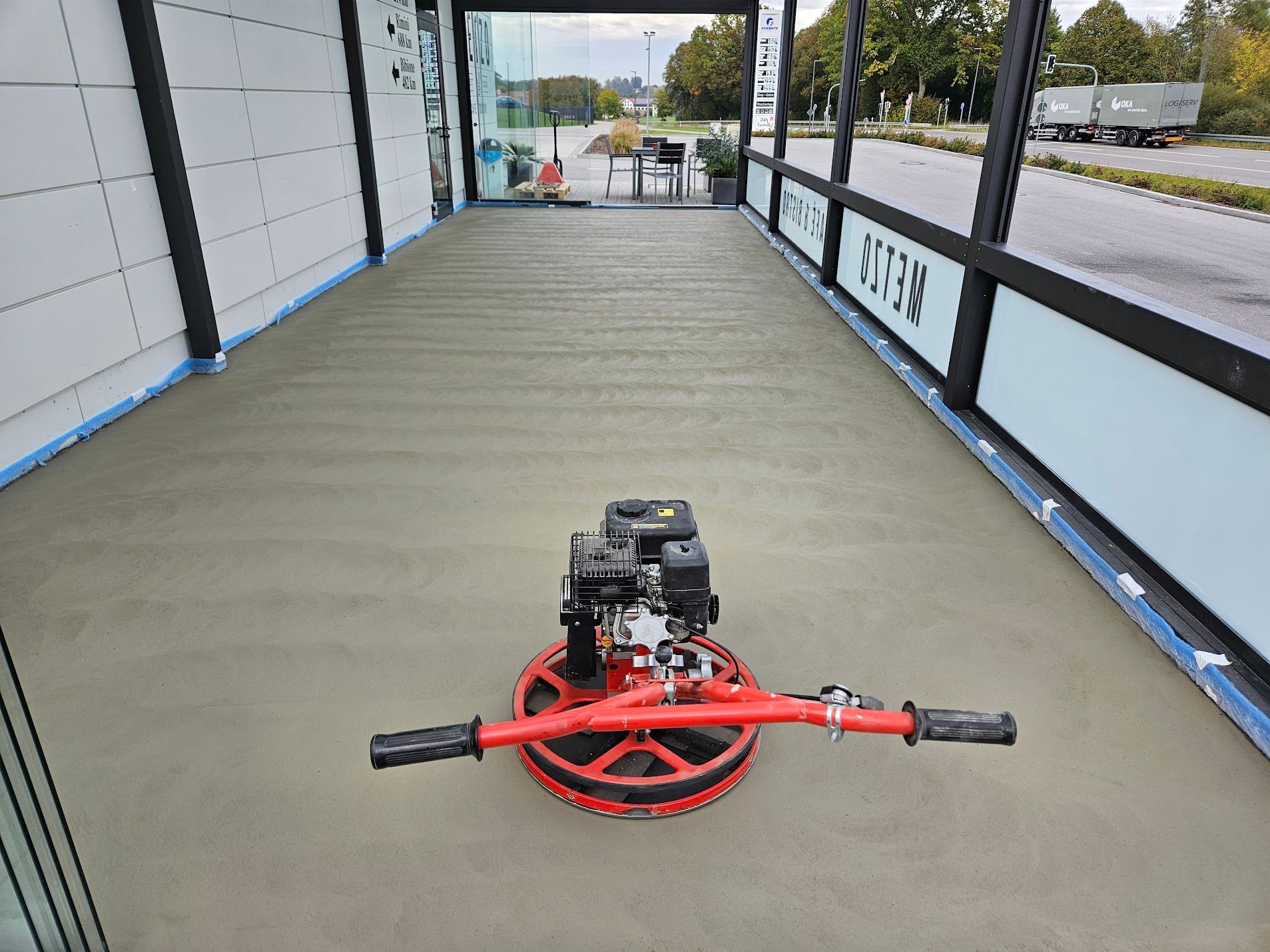 Ein Arbeiter glättet einen hellbeigen Epoxidharzboden in einem Raum mit schrägen Decken, hellen Wänden und einem Fenster.