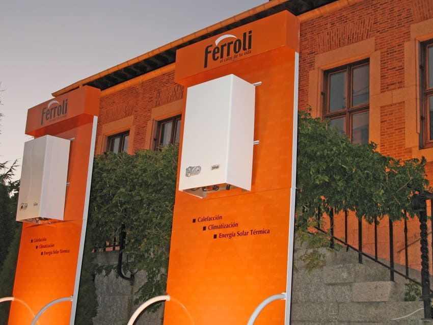 Expositores naranjas con calderas Ferroli blancas, delante de un edificio naranja.