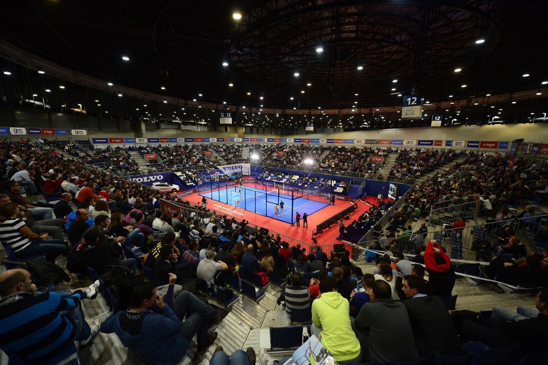Tres mujeres con atuendos iguales posan junto a un anuncio de Ferroli. Llevan faldas negras, camisas blancas y pañuelos naranjas.
