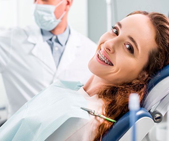 Una mujer con aparatos ortopédicos sonríe mientras está sentada en una silla dental.