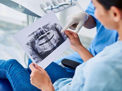 Una mujer está sentada en una silla dental mirando una radiografía de sus dientes.