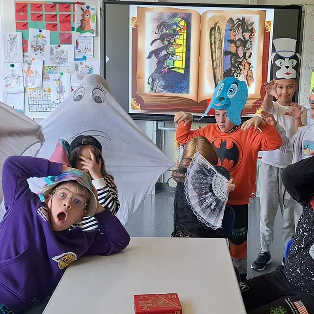 Kinder in Kostümen posieren für ein Foto in einem Klassenzimmer, auf dessen Bildschirm eine Bilderbuchillustration zu sehen ist.