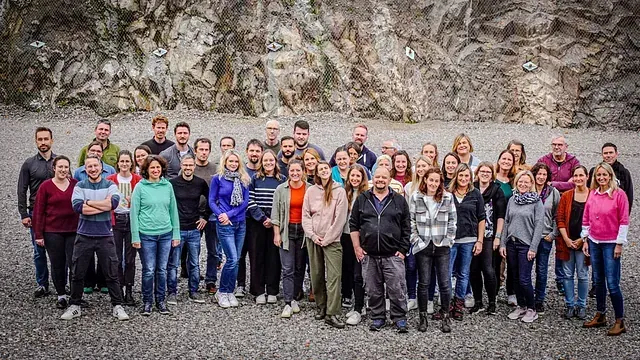 Eine Gruppe von Menschen steht vor einer Felswand. Viele lächeln.