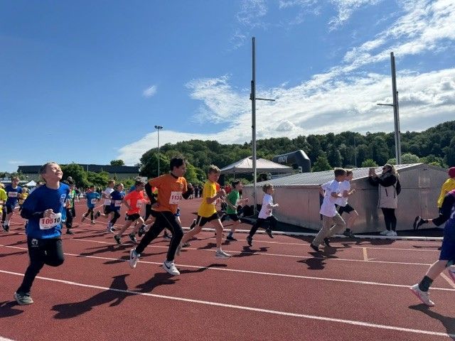 Runners in colorful shirts racing on an outdoor track under a bright blue sky
