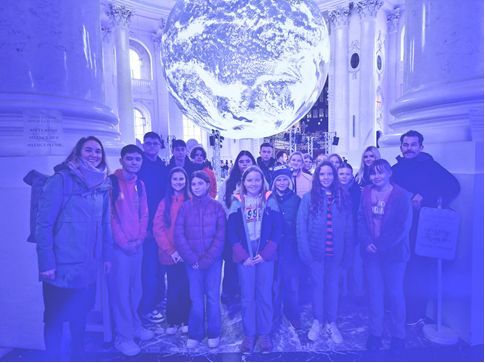 Eine Gruppe von Menschen posiert vor einem riesigen Globus in einem Gebäude mit Säulen.