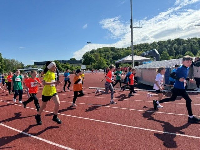 Runners in colorful shirts sprint on a track during a sunny outdoor race event