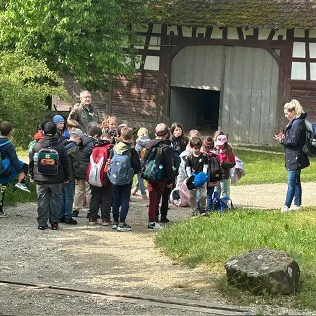 Kinder bei einem Schulausflug vor einer Scheune; Erwachsene begleiten sie.