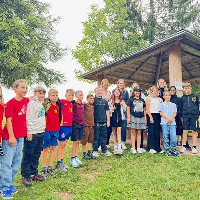 Gruppe von Kindern und Erwachsenen posiert im Freien unter einem Holzunterstand.