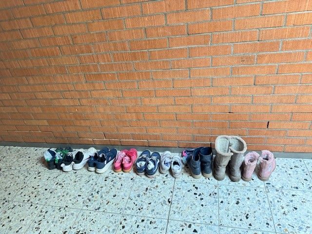 Schuhe, aufgereiht an einer Backsteinmauer auf einem gefliesten Boden.