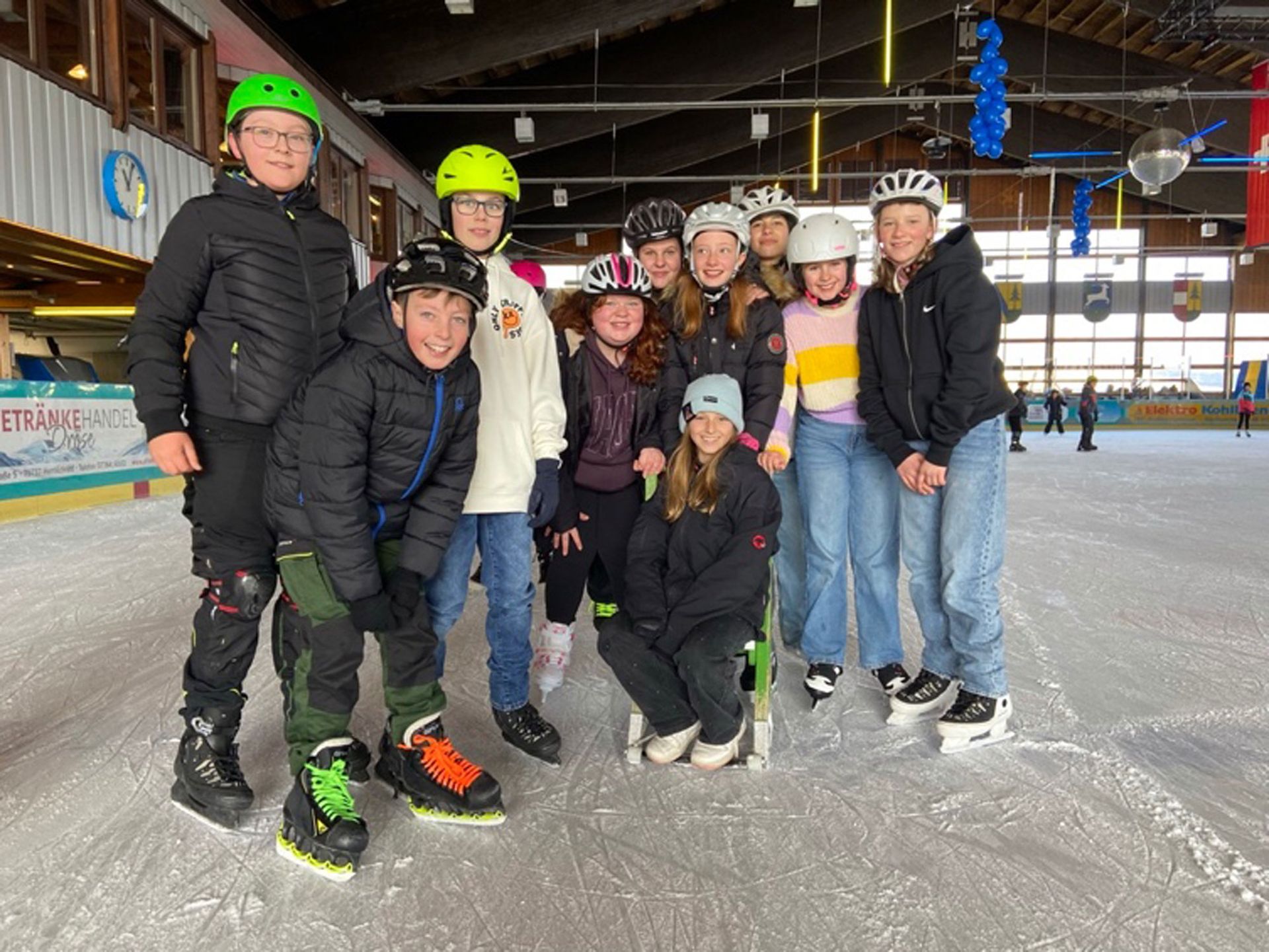 Eine Gruppe von Menschen mit Helmen posiert auf einer Eisbahn.