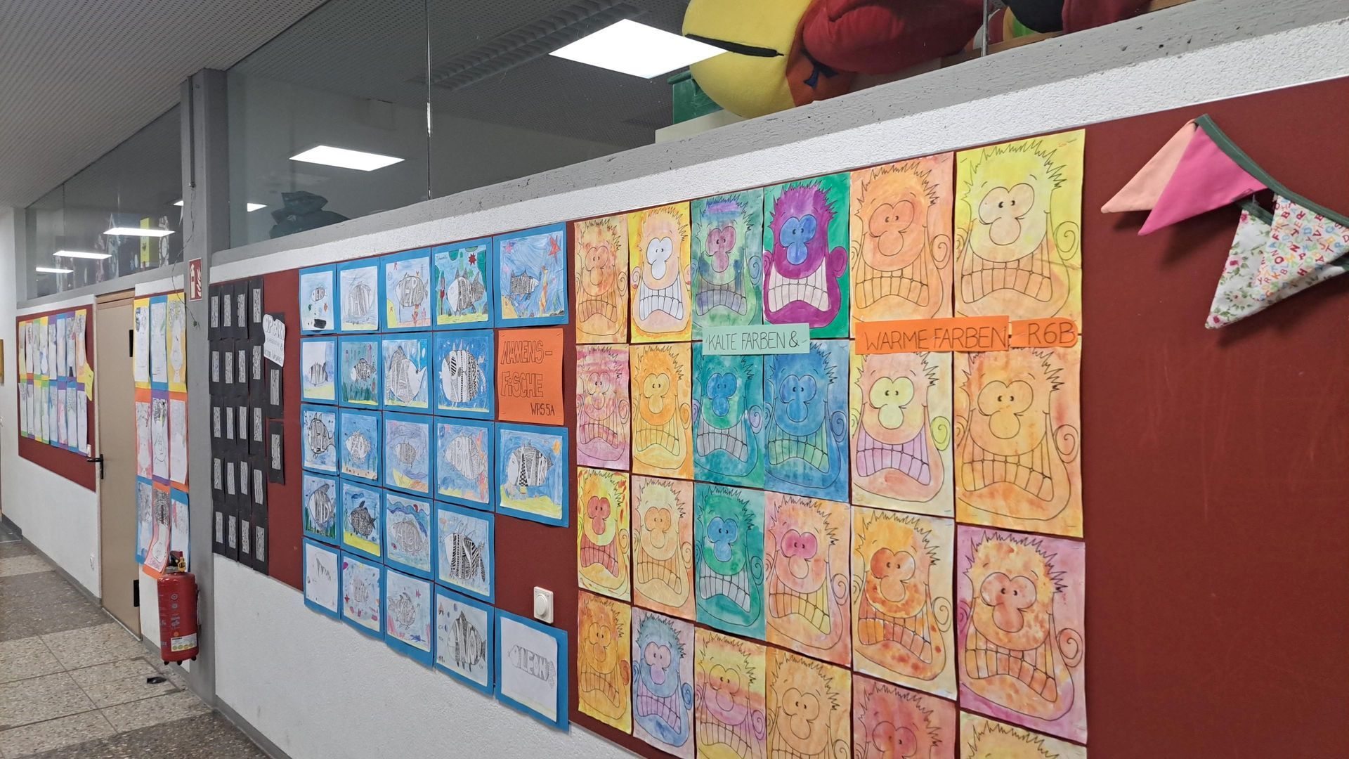 Flur mit Kinderzeichnungen an einer roten Wand; Licht von der Decke, verschiedene bunte Bilder.