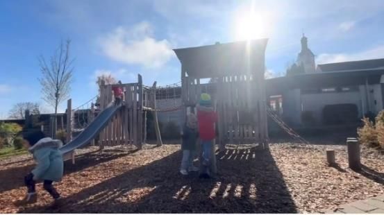 Kinder spielen unter strahlend blauem Himmel auf einem Spielplatz mit Rutsche und Klettergerüst.