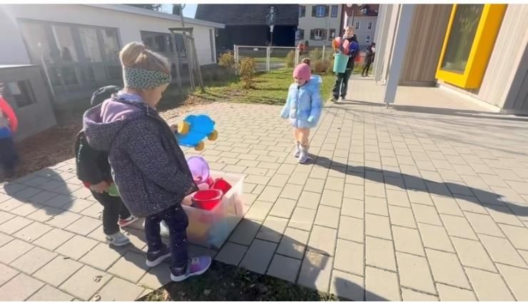 Kinder spielen draußen vor einem Gebäude mit Spielzeug und Luftballons. Sonniger Tag.