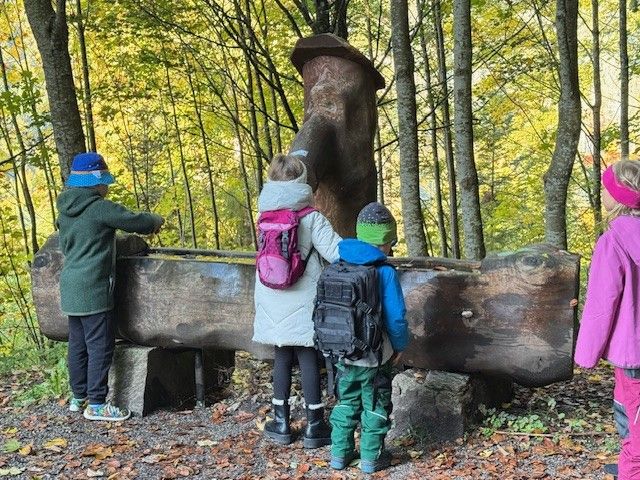 Kinder an einem hölzernen Wasserbrunnen im Wald. Herbstlaub.