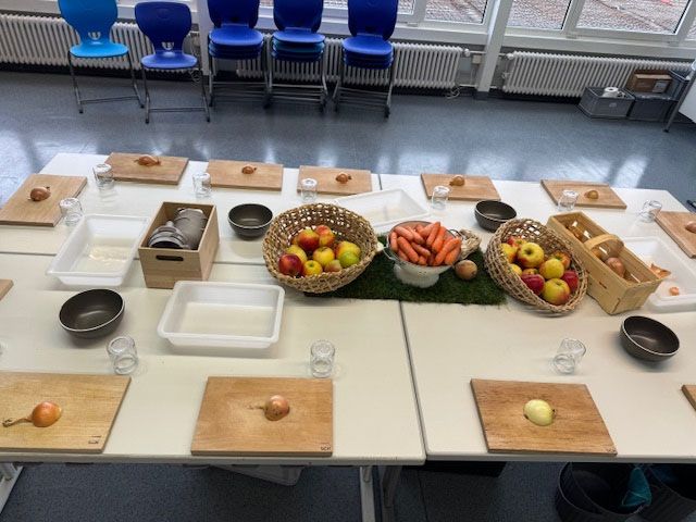 Ein mit Lebensmitteln, Schneidebrettern und Schüsseln gedeckter Tisch, möglicherweise für eine Kochvorführung oder einen Kochkurs.