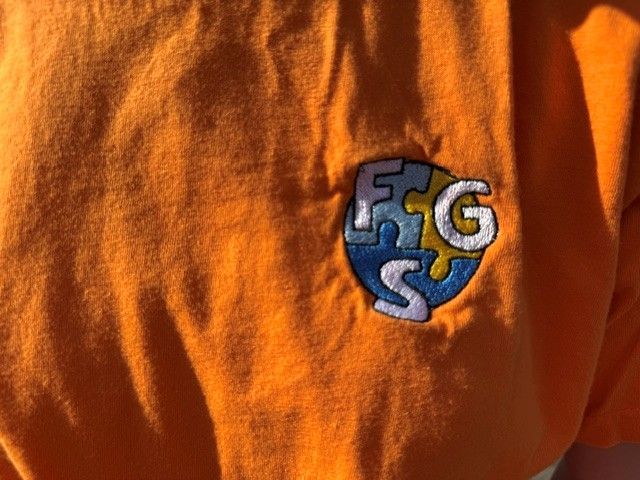 Orange shirt with a small embroidered blue-and-white shield logo on the chest