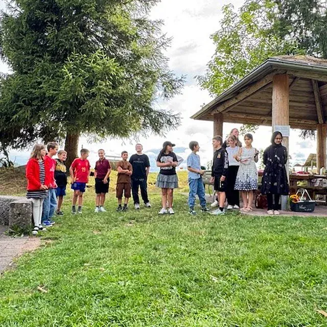 Eine Gruppe Kinder steht auf einer Wiese neben einem Pavillon. Einige schauen in die Kamera. Bewölkter Himmel.
