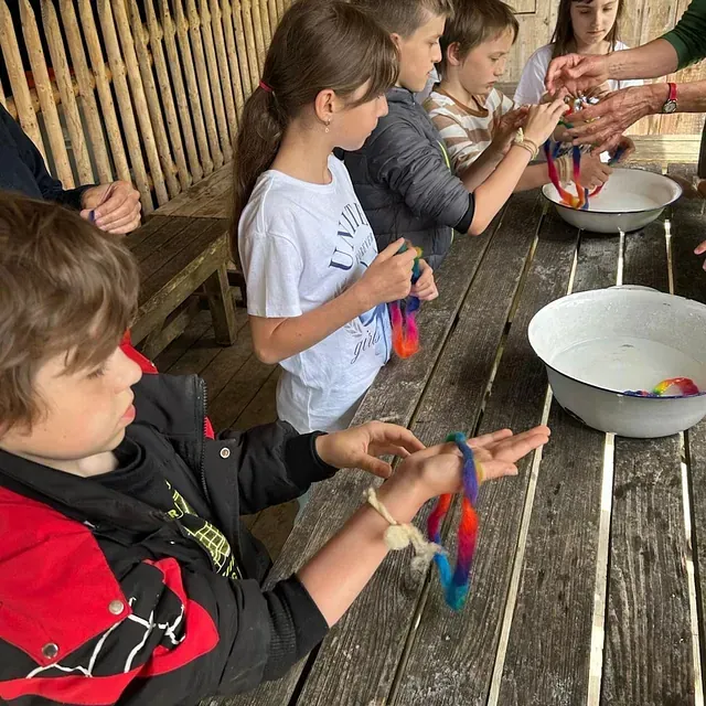 Kinder basteln und tauchen bunte Wollknäuel in Wasserschüsseln auf einem Holztisch im Freien.