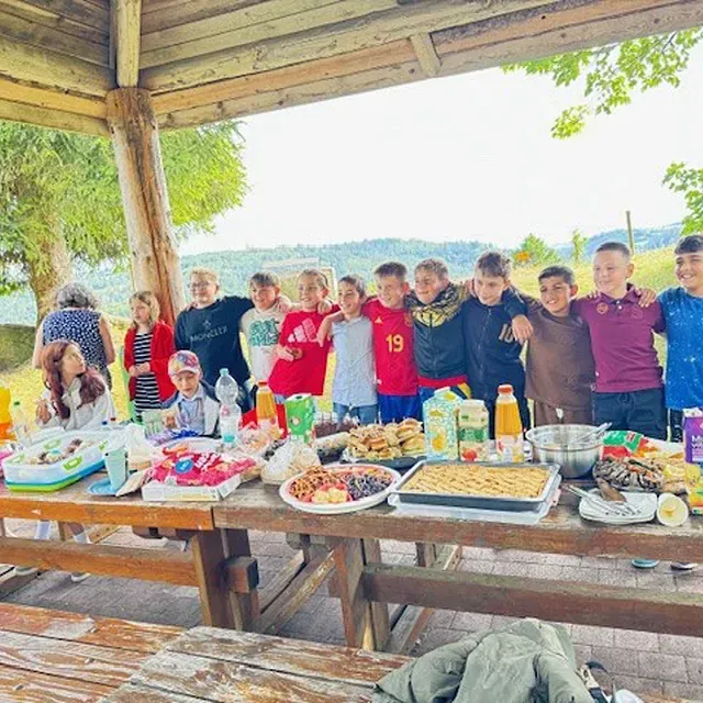 Kinder an einem Picknicktisch mit Essen und Getränken; sie lächeln und posieren draußen für ein Foto.