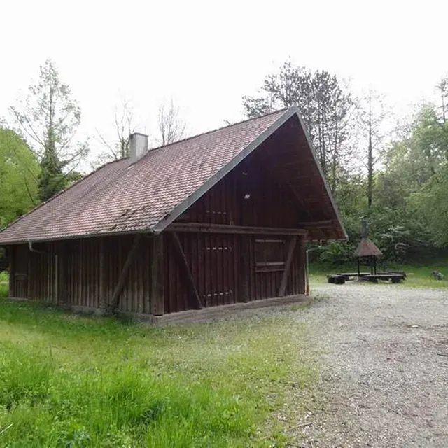 Eine Holzhütte mit Ziegeldach auf einer grasbewachsenen Lichtung mit einem Picknicktisch.