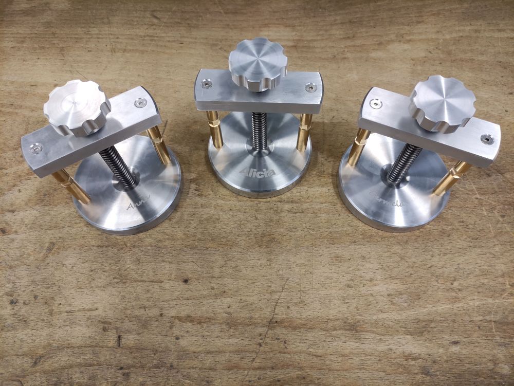 Three small silver metal clamp-like fixtures on a wooden surface, each with a round base and knob on top
