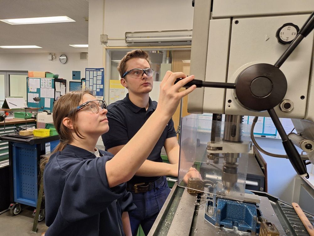 Two technicians inspect and adjust a machine in a workshop lab.