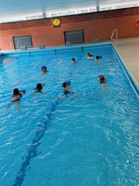 Kinder mit Badekappen und Schwimmflügeln in einem Schwimmbecken lernen schwimmen.