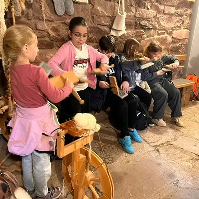 Kinder lernen, Wolle an einem Spinnrad und mit Spindeln im Haus zu spinnen.