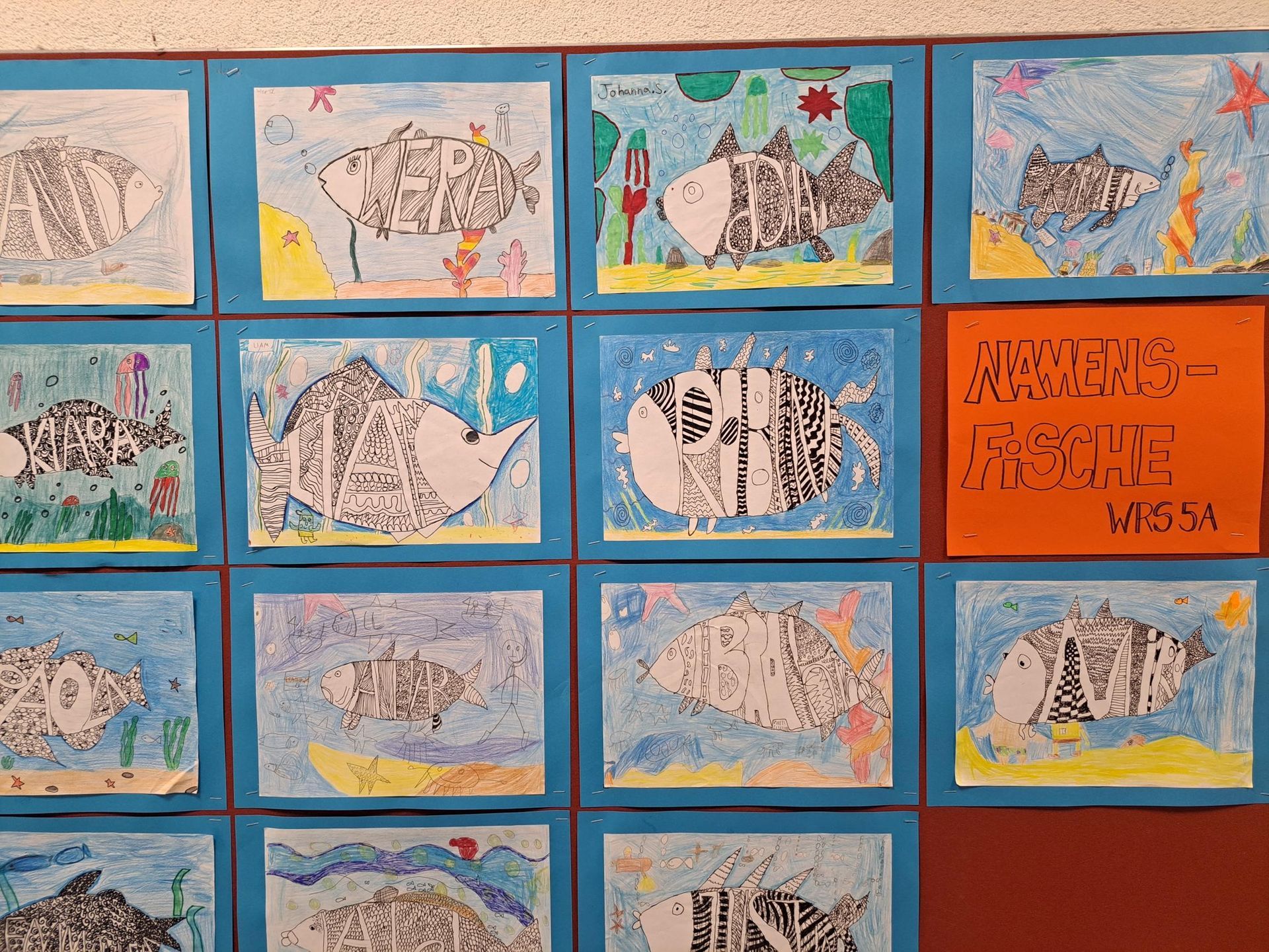 Ausstellung von schwarz-weißen Fischen vor blauem und gelbem Hintergrund, Schülerarbeiten.