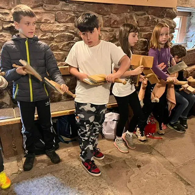 Kinder halten Holzpaddel in einem Steingebäude. Sie scheinen nach vorne zu blicken.