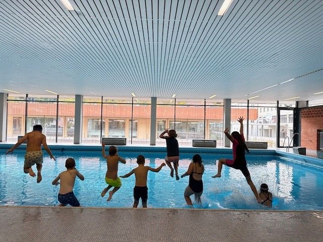 Kinder springen in einem Hallenbad in ein Becken. Blaues Wasser, helle Decke.