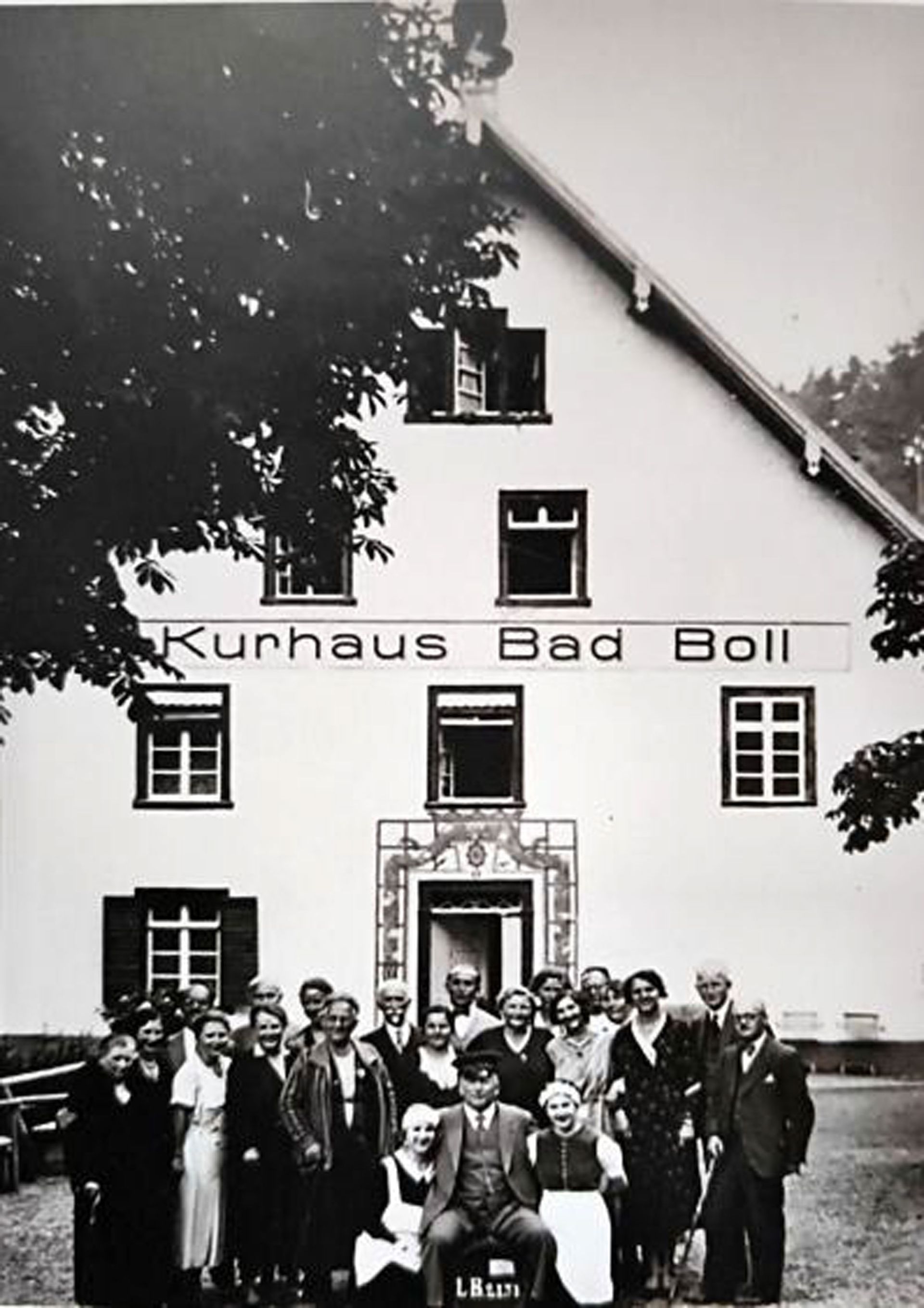 Eine Gruppe von Menschen posiert vor dem „Kurhaus Bad Boll“, einem Gebäude mit Schild. Schwarz-Weiß-Foto.