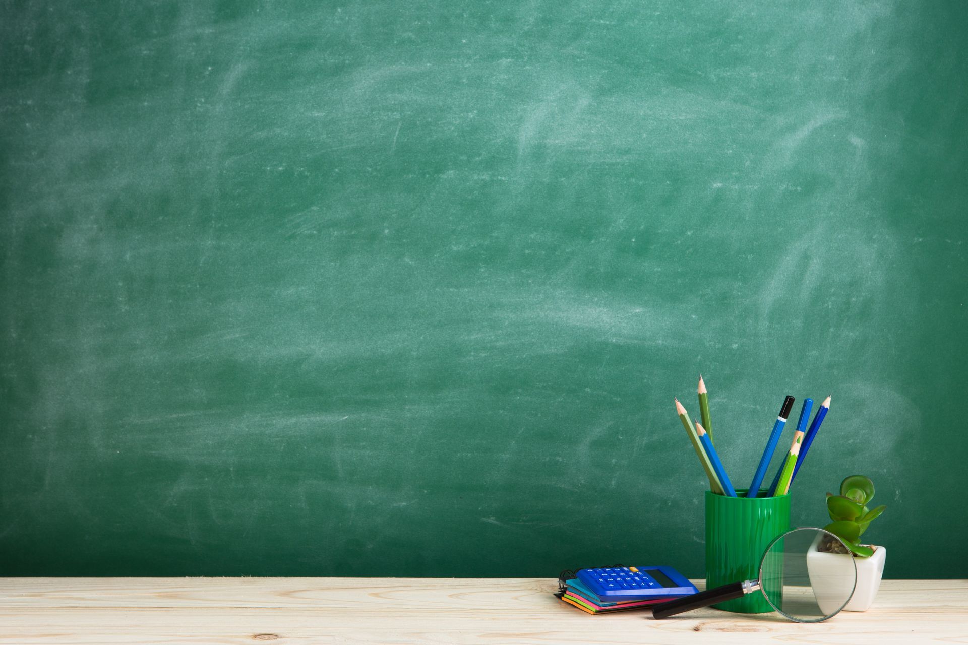 Grüne Tafel mit Stiften, einer kleinen Pflanze und anderen Utensilien auf einer Holzoberfläche.