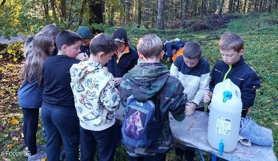 Eine Gruppe Kinder sitzt draußen um einen Tisch und betrachtet etwas. Ein Wasserkrug steht daneben.