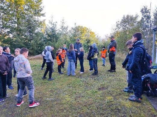 Eine Gruppe von Kindern und Erwachsenen, einige trugen orangefarbene Westen, hatte sich im Freien auf einer Wiese versammelt.