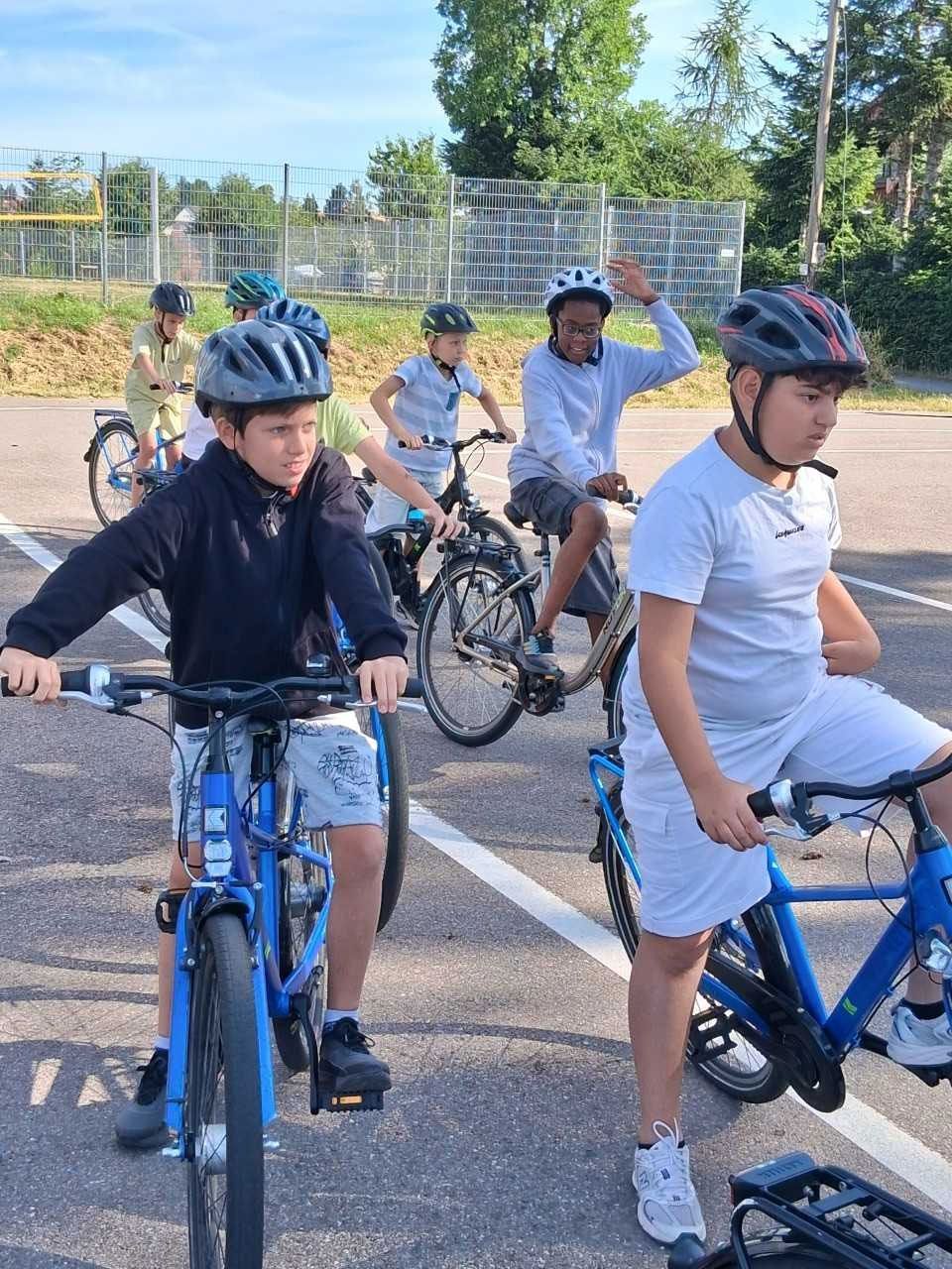 Kinder auf blauen Fahrrädern mit Helmen standen draußen auf einem sonnigen, gepflasterten Weg.