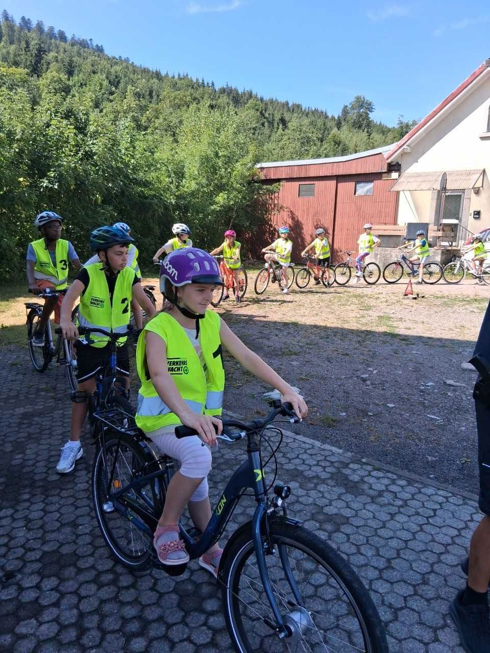 Radfahrer in Warnwesten und Helmen bereiten sich vor einem Gebäude am Waldrand auf eine Fahrt vor.