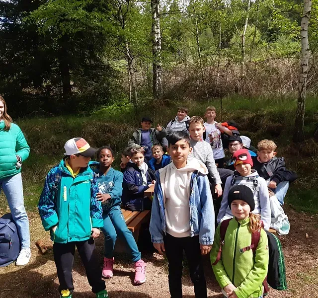 Eine Gruppe Kinder hatte sich im Freien in einem Waldstück versammelt, einige saßen auf einer Bank.
