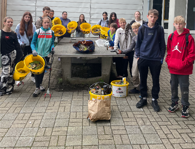 Eine Gruppe Jugendlicher mit Eimern reinigt draußen einen Betontisch, auf dem Müll gesammelt ist.